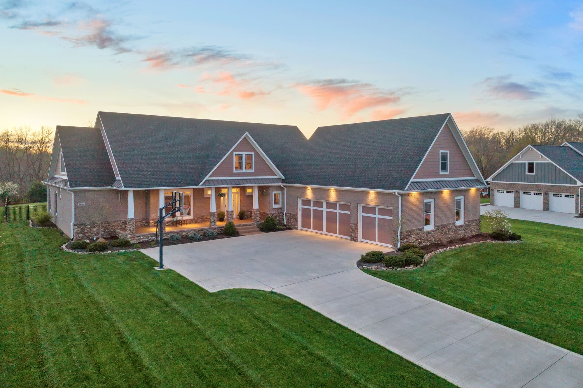 Golden hour aerial of a ranch home with a wide concrete driveway at sunset