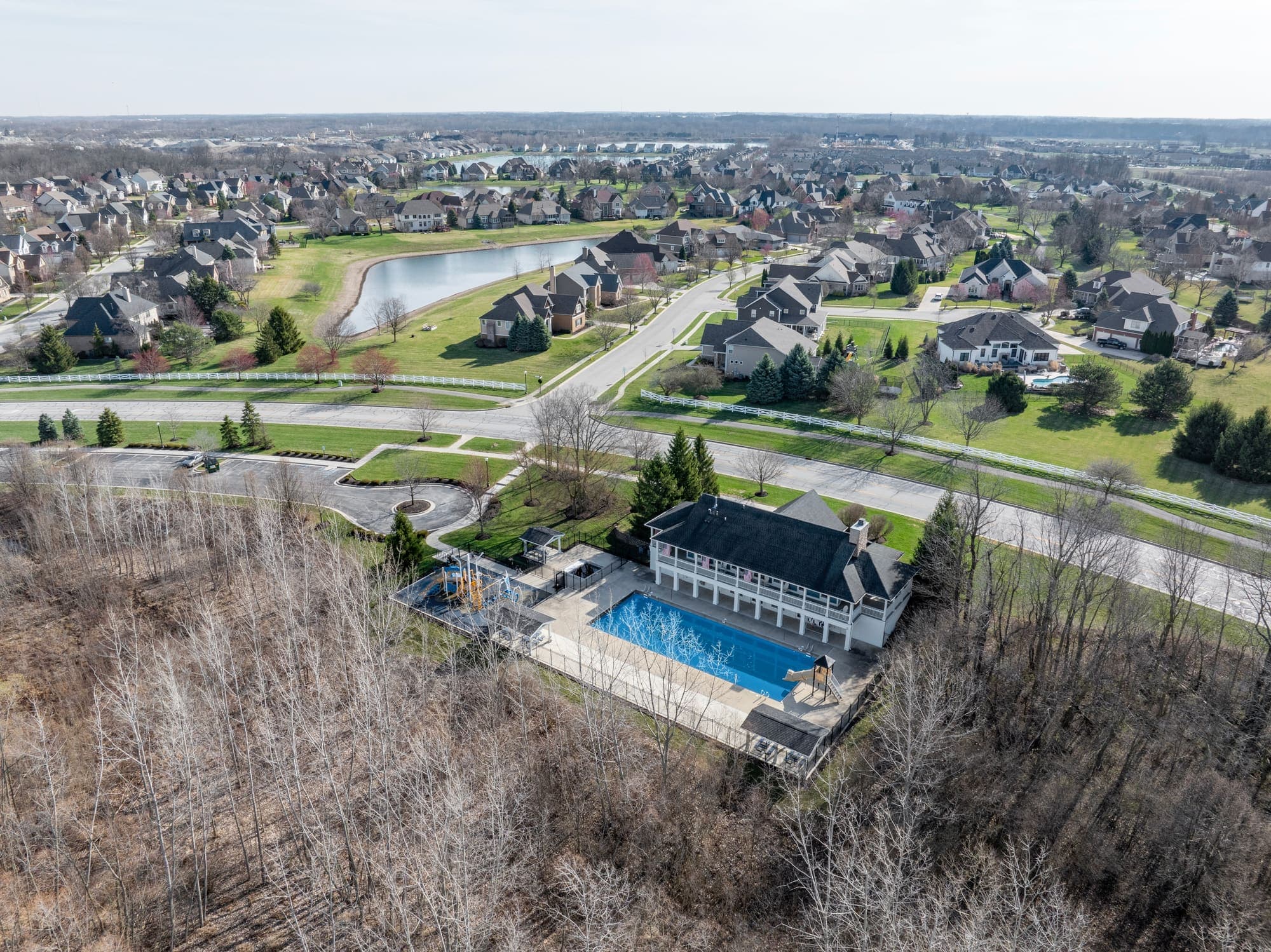 High aerial of a lakeside neighborhood with ponds, a community pool, and tree-lined streets
