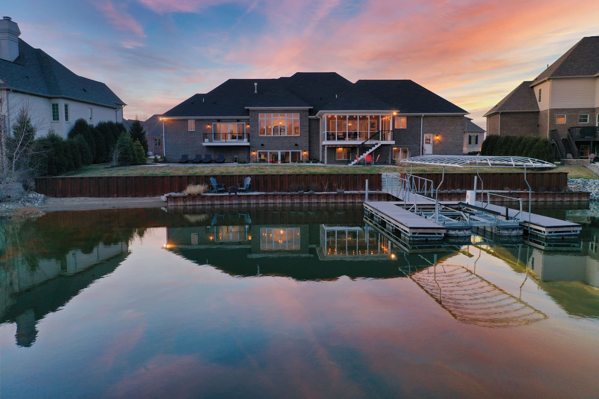 Twilight aerial of a lakeside home with dock and boat lifts mirrored in still water